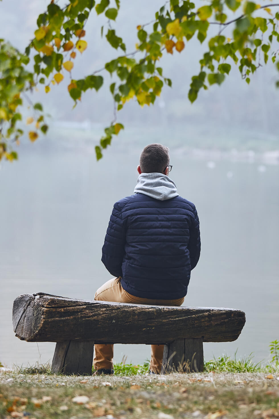 Grieving man sits on bench overlooking the water.