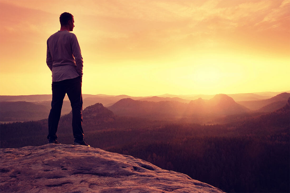 Grieving man on mountaintop takes in the sunrise.