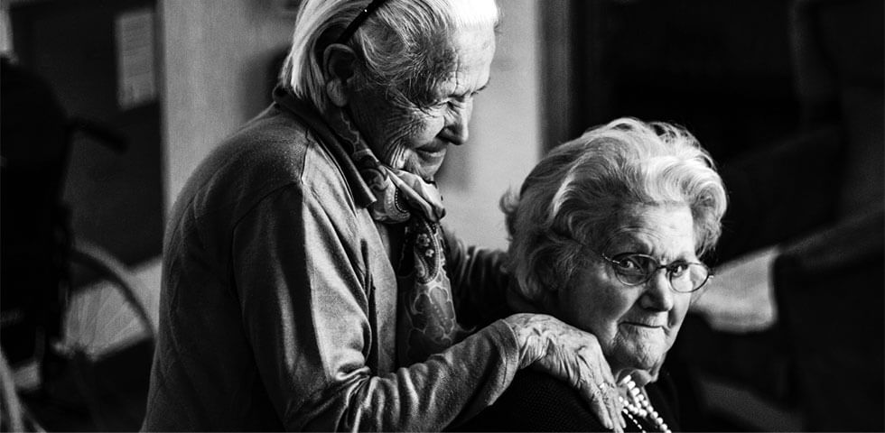 Two elderly women supporting each other.