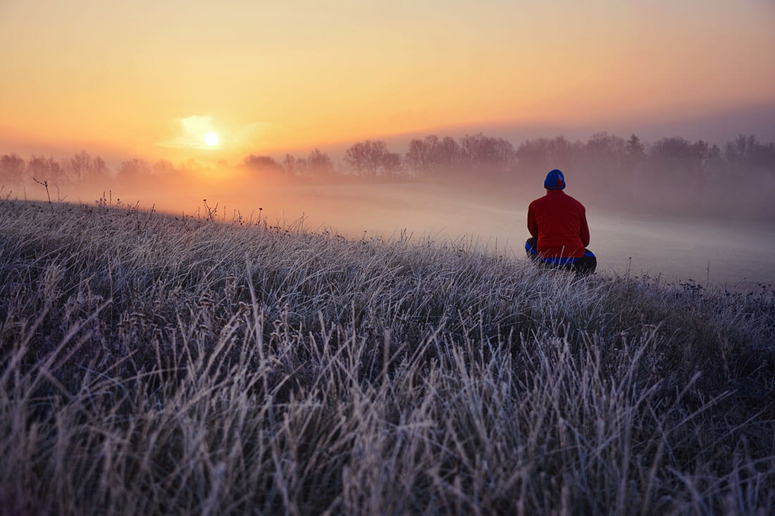 Young man standing in winter frozen nature and watching to the calm winter misty sunrise