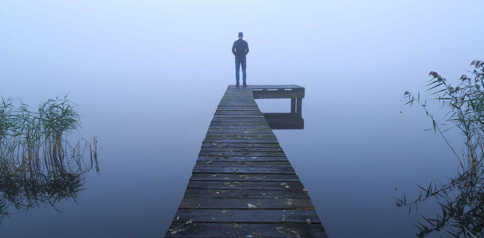 Grieving man stands at end of dock on a foggy day.