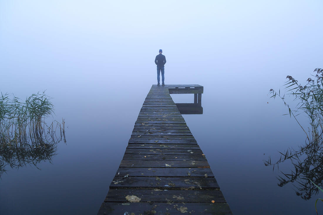 Man stands at end of dock on a foggy day.