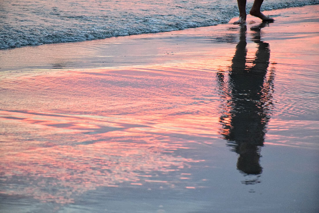 Reflection of person walking along the shore during the sunset.