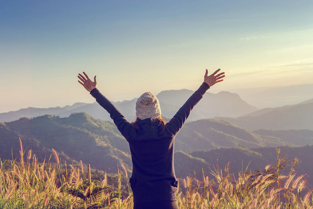 Woman celebrates summiting a mountain and takes in the view.