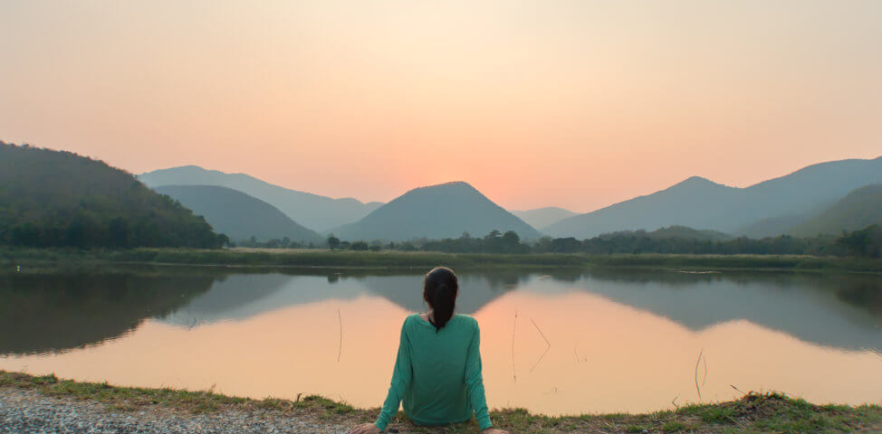 Woman sits peacefully at a lake watching sunset