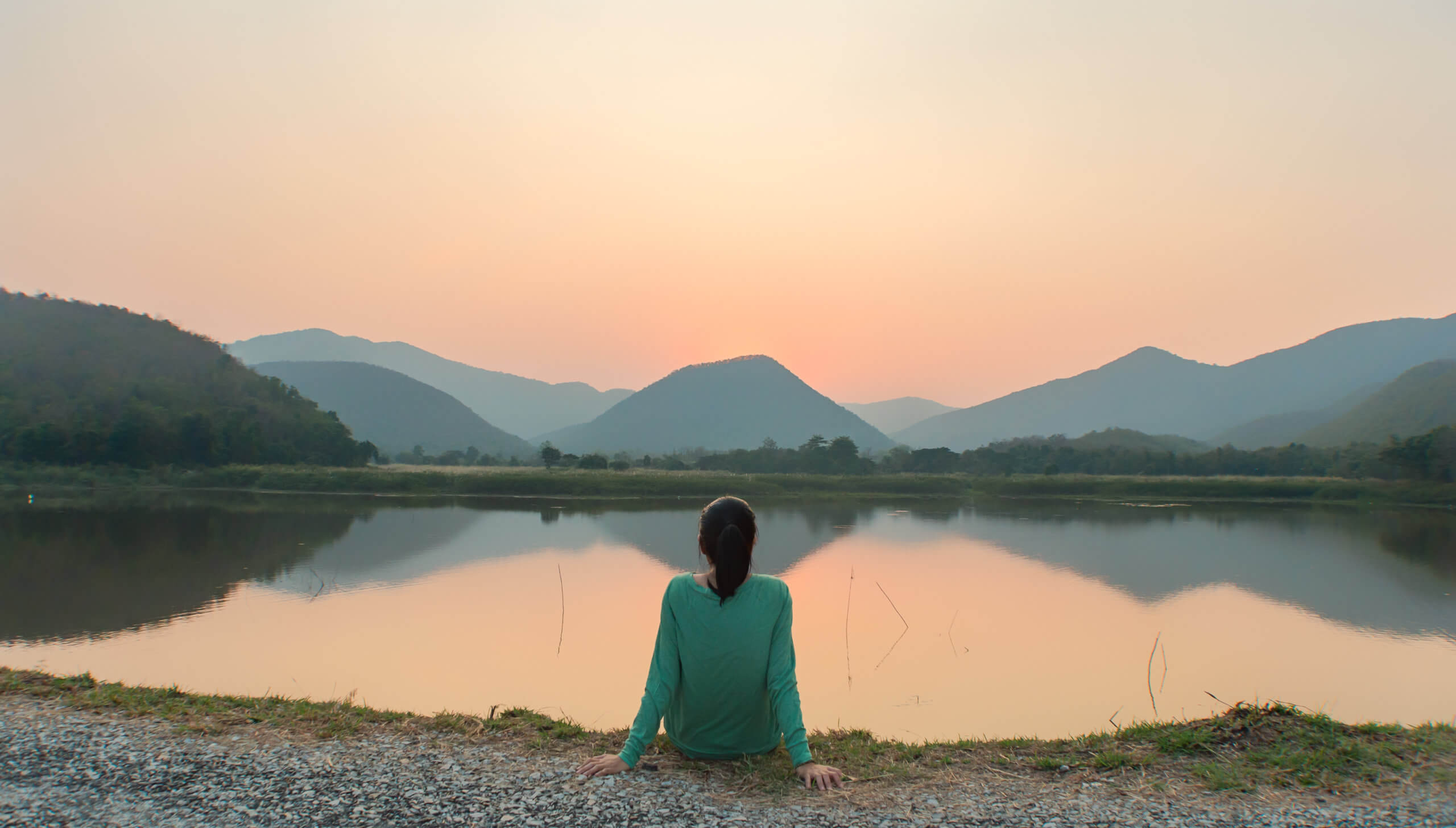 Woman sits peacefully at a lake watching sunset